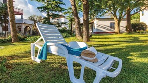 A white plastic lounge chair with a towel and a straw hat on it, placed on a grassy lawn with trees and buildings in the background. - 2 bedroom pet friendly home in Medulin (Medulin)