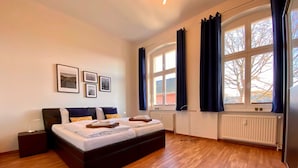 Une chambre à coucher avec un grand lit, une table de chevet, un radiateur et une fenêtre avec des rideaux.