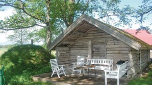 A rustic wooden cabin with a pitched roof, a small porch area with white metal chairs and a table, surrounded by greenery. - 1 bedroom amazing home in Brålanda (Brålanda)