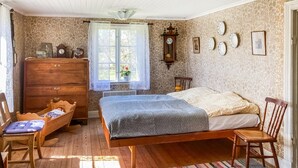 A bedroom with a wooden bed, a wooden dresser, a chair, a window with lace curtains, and a wall clock. - 1 bedroom amazing home in Brålanda (Brålanda)