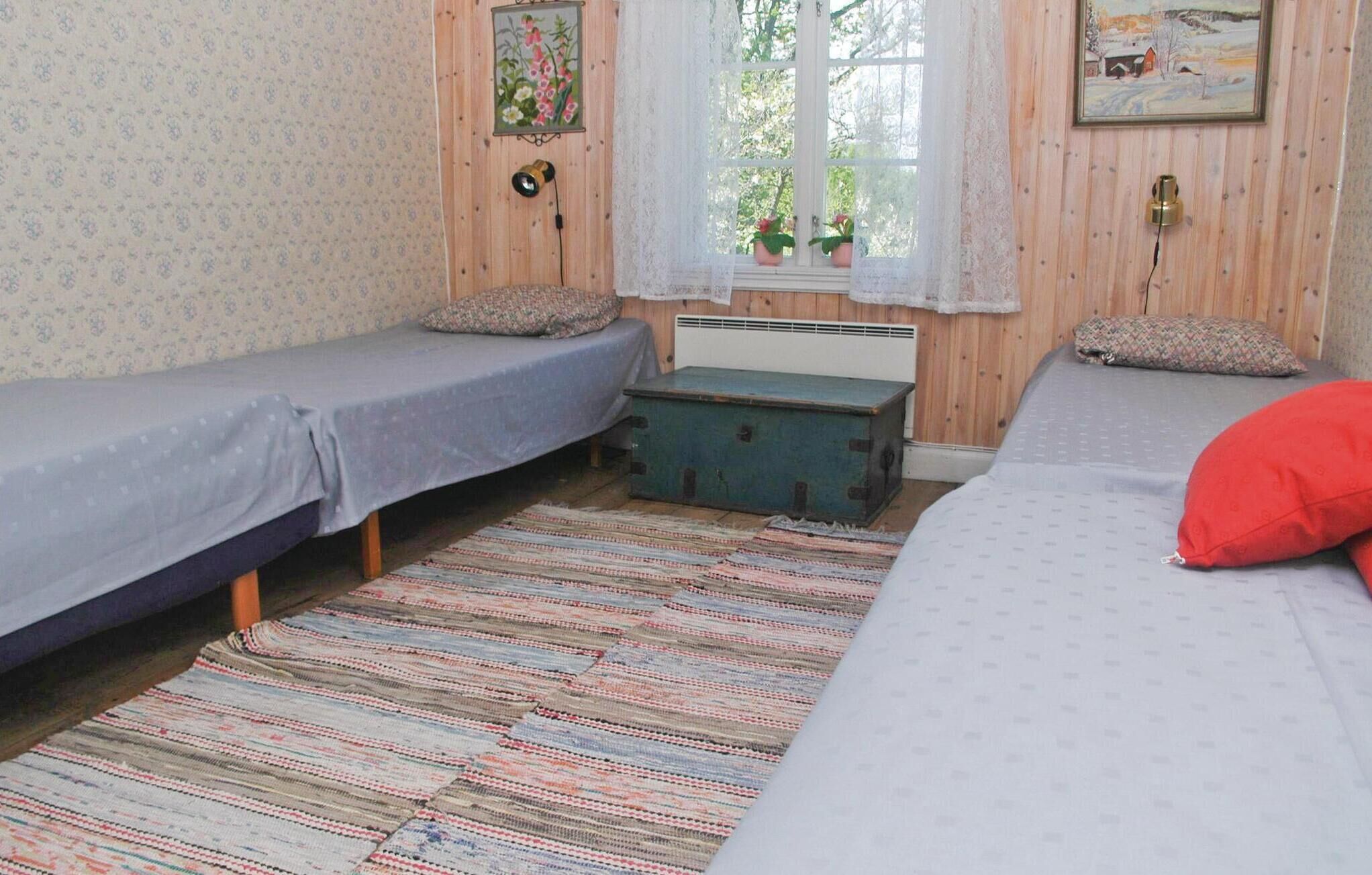 Ein Zimmer mit zwei Einzelbetten, einem kleinen Tisch und einem Fenster mit Blick auf Bäume.