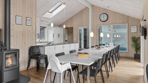 A modern kitchen with a central island, a dining area with a long table and chairs, a built-in stove, and a large window providing natural light. - Beautiful home in ålbæk with kitchen (Ålbæk)