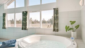 A bathroom with a large bathtub, a window with patterned curtains, and a potted plant. - Beautiful home in ålbæk with kitchen (Ålbæk)