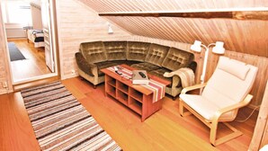 A cozy attic room with a curved sectional sofa, a small wooden table, a white armchair, and a slanted ceiling. - 3 bedroom amazing home in Svenljunga (Svenljunga)