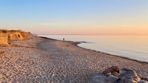 Ein sandiger Strand mit blauem Himmel und ruhigem Wasser.