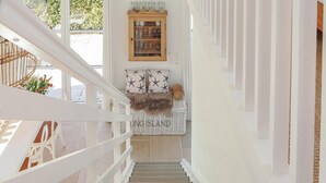 Eine Treppe mit weißer Reling, ein Korbwesen mit Blumen, eine Vitrine mit Glaswaren und eine Wand mit Kissen mit Sternenmuster.