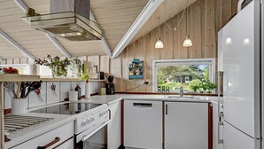 A modern kitchen with white cabinetry, a built-in oven, a dishwasher, and a window offering a view of the outdoors.