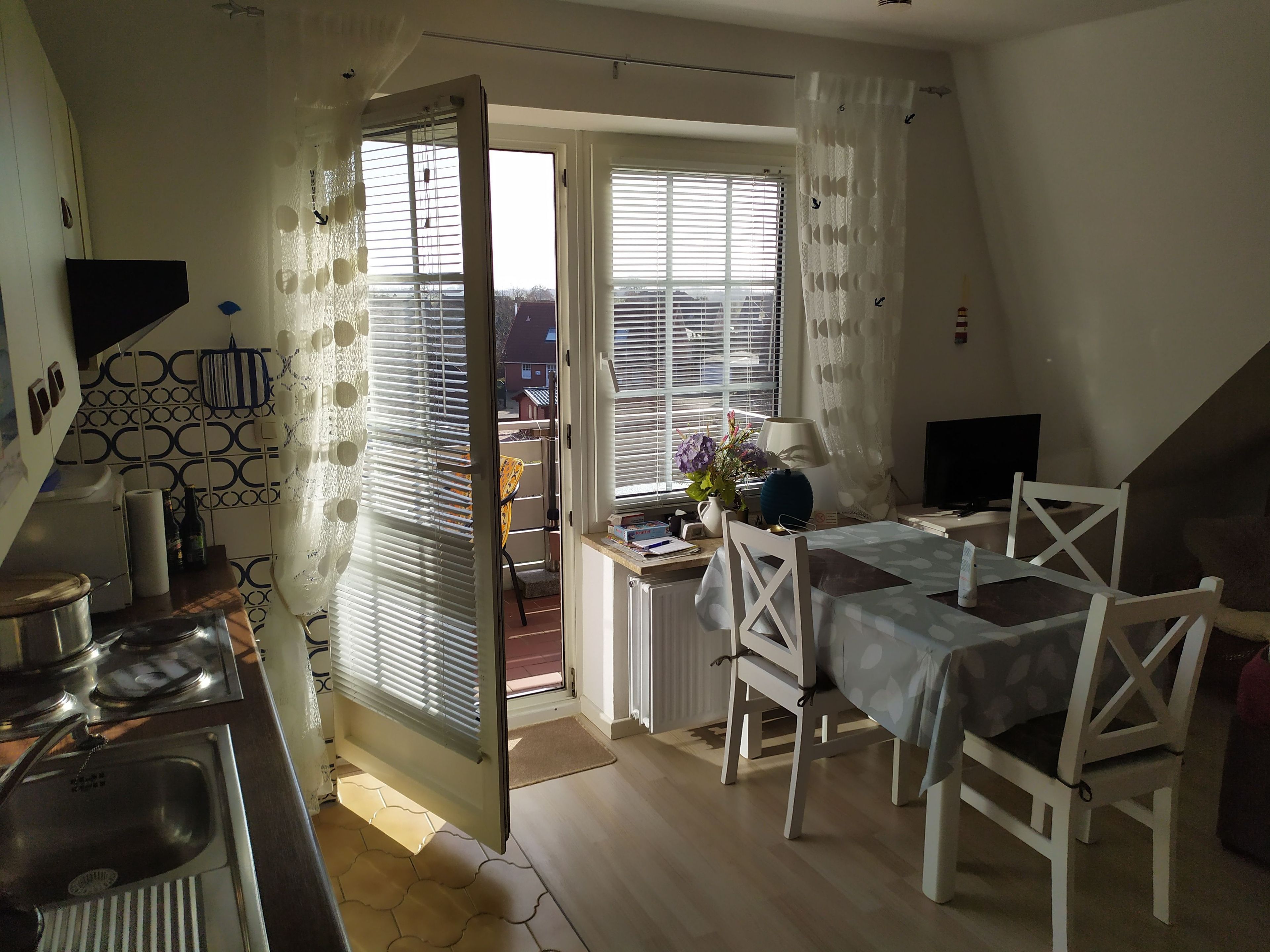 Een gezellige, goed verlichte kamer met een keukenhoek, een eettafel met stoelen, een televisie en uitzicht buiten door grote ramen.