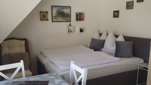 A small, well-lit room with a bed, a dining table, and a chair. There are wall decorations and a picture frame. - Apartment Fofftein (Friedrichskoog)