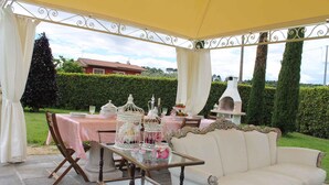An outdoor patio with a table set for a meal, a white sofa, and a decorative birdcage. - Holiday apartment mit Pool (Montecarlo Lucca)