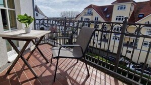 A balcony with a table and chair, a potted plant, and a view of neighboring buildings. - (91) 3-room apartment south-facing balcony - apartment house Atlantic (Kühlungsborn)
