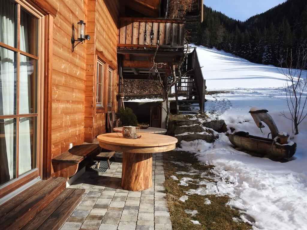A wooden cabin with a stone fireplace, a wooden deck, and a snowy landscape in the background.