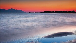 Rustig wateroppervlak dat een zonsondergang weerspiegelt, met bergen op de achtergrond.