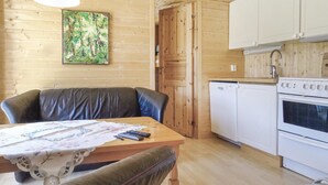Ein gemütliches Blockhaus-Interieur mit einem Esstisch, Ledersesseln, einer Küchenzeile mit Herd und Kühlschrank sowie einer Holzwand mit einem gerahmten Gemälde.