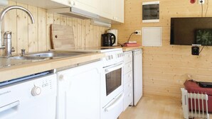 Eine kleine Küche mit Spüle, Herd und Backofen, Holzwänden und einem kleinen Fernseher an der Wand.