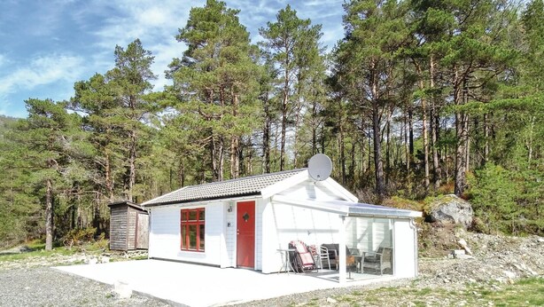 Eine kleine, eingeschossige Holzhütte mit roter Tür und weißen Wänden, umgeben von einem Wald.