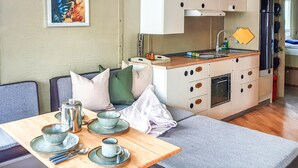Une petite cuisine équipée comprenant un évier, une cuisinière et des placards. Un coin repas est aménagé avec une table pour deux personnes, comprenant des assiettes, des bols et des tasses.