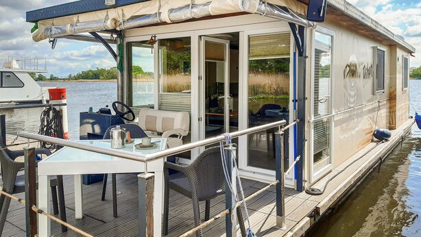 Une péniche dotée d’une terrasse couverte, d’une table avec des chaises et d’un volant.