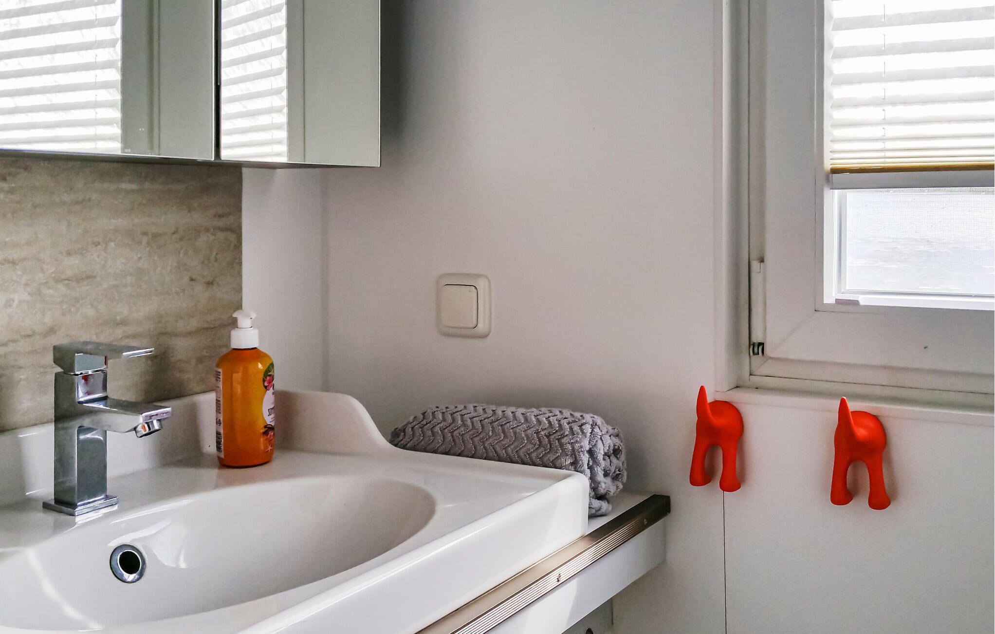 A bathroom with a white sink, a chrome faucet, a bottle of orange liquid, a gray towel, and two red animal-shaped bath accessories.