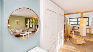 Een kamer met een ronde spiegel, een bank, een klein tafeltje, een wit kastje met decoratieve panelen en een rieten stoel.