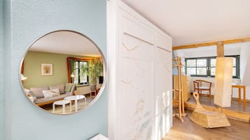 A room with a round mirror, a sofa, a small table, a white cabinet with decorative panels, and a wicker chair.