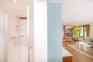 Une salle de bain avec une douche, des toilettes et un lavabo. Il y a un salon avec un canapé, une table basse et un téléviseur.