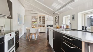 Une cuisine moderne dotée d’un îlot central, de meubles blancs et d’une grande fenêtre qui laisse entrer la lumière naturelle.