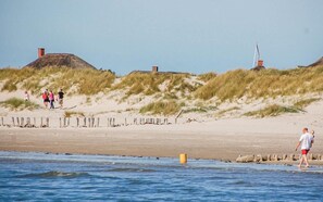 A beach with dunes, a lighthouse, and a wooden fence.