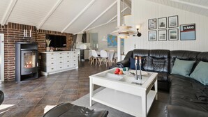 Un salon chaleureux avec une cheminée, un canapé en cuir noir et un coin repas agrémenté d’une carte au mur.