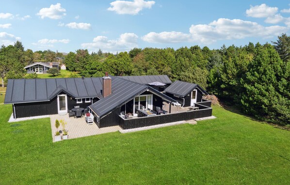 A modern house with a large patio area, a covered outdoor seating area, and a well-maintained lawn.
