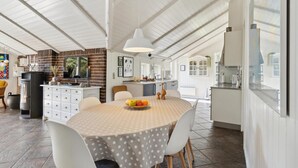 Une cuisine spacieuse avec des meubles blancs, un mur décoratif en briques et un grand îlot central doté d’un évier et d’un plan de travail.