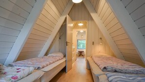 Ett litet, mysigt sovrum på vinden med två enkelsängar, träribbor i taket och en smal hall som leder till ett fönster.