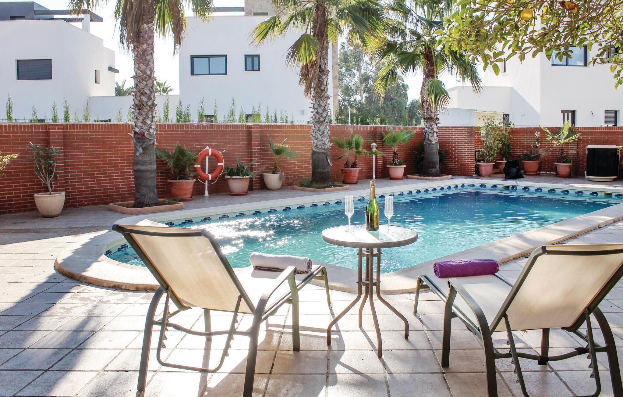 A swimming pool with lounge chairs and a table, surrounded by potted plants and a brick wall.