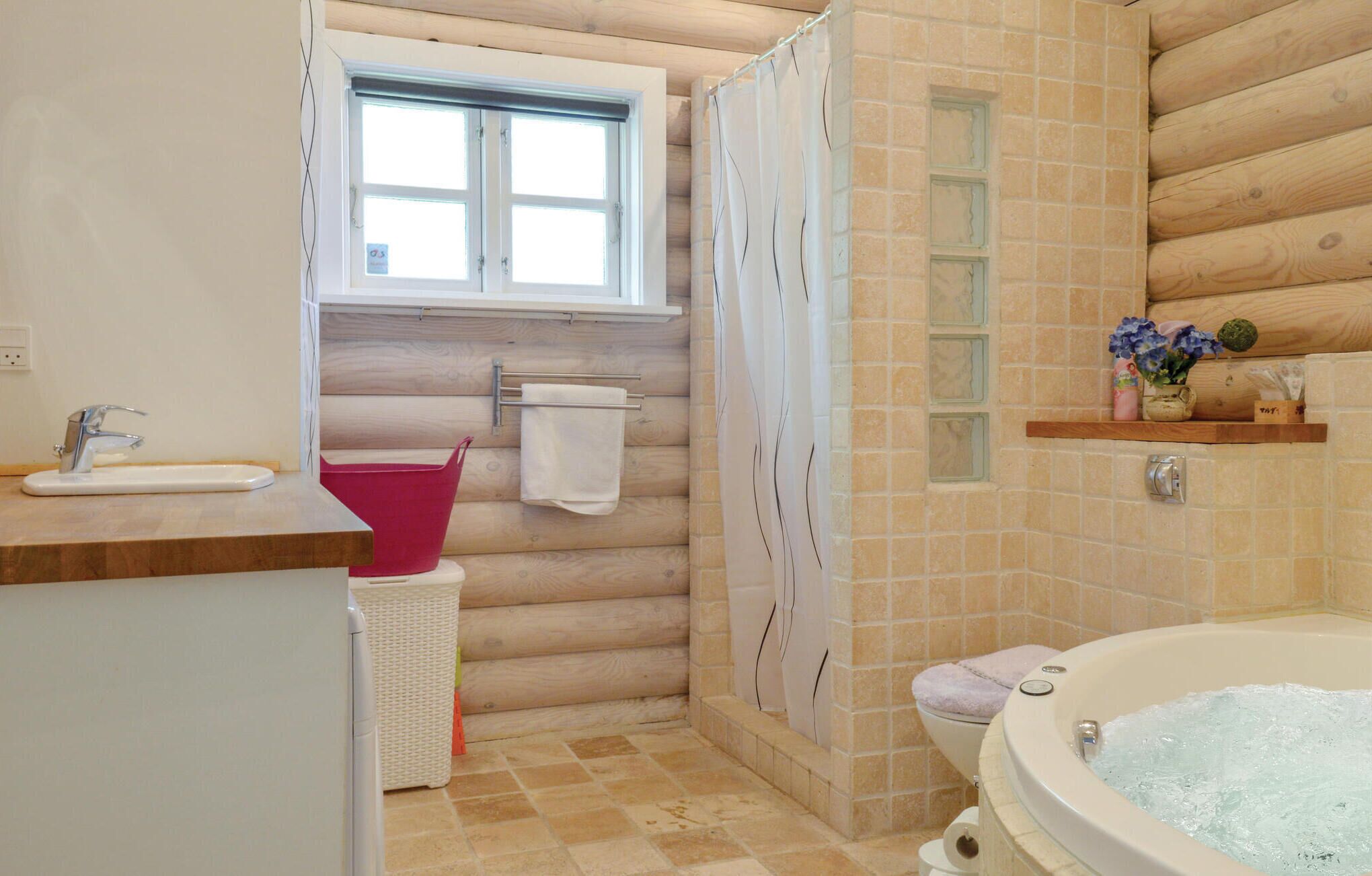 A bathroom with a wooden interior, a bathtub, a shower curtain, a window, a sink, and a toilet.
