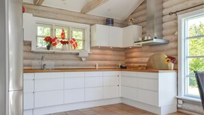 Une cuisine moderne avec des meubles blancs, un plan de travail en bois et une grande fenêtre donnant sur un paysage verdoyant.