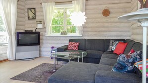Un salon chaleureux avec un canapé gris, une table basse en verre, un téléviseur à écran plat et une fenêtre avec des rideaux.