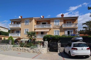 A multi-story residential building with balconies, a gated entrance, and a parked car.