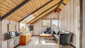 Ein gemütliches Zimmer im Dachgeschoss mit schrägen Wänden, Holzwänden, einer schwarzen Ledersofa, einem Holztisch und einer kleinen Küchenzeile mit Spüle und Schränken.