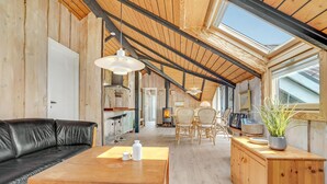 Ein gemütliches Loft mit Holzbalkendecke, einer schwarzen Ledersofa, einem Holzesstisch und einer Küchenzeile mit Kaminofen.