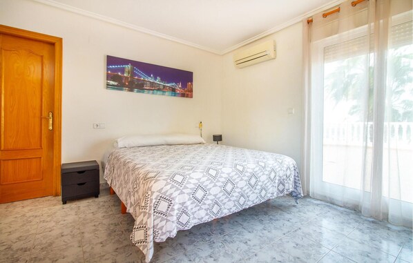 Une chambre à coucher comprenant un lit, une table de chevet, un climatiseur fixé au mur et une fenêtre avec des rideaux.