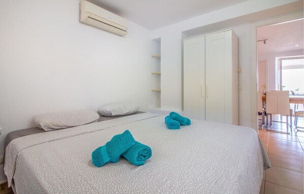 Un dormitorio con cama, dos almohadas, una toalla doblada, un equipo de aire acondicionado, un armario y una puerta que da a un balcón.