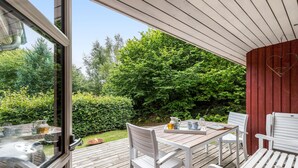 An outdoor patio with a wooden deck, white furniture, and a view of a lush green garden. - Cozy home in Ebeltoft with WiFi (Ebeltoft)