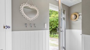 A hallway with a heart-shaped mirror, three flower-shaped wall hooks, a hat on a rack, and a door leading outside. - Cozy home in Ebeltoft with WiFi (Ebeltoft)