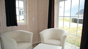 Une pièce avec deux fauteuils blancs et une table blanche, des murs lambrissés en bois et de grandes fenêtres avec des rideaux.