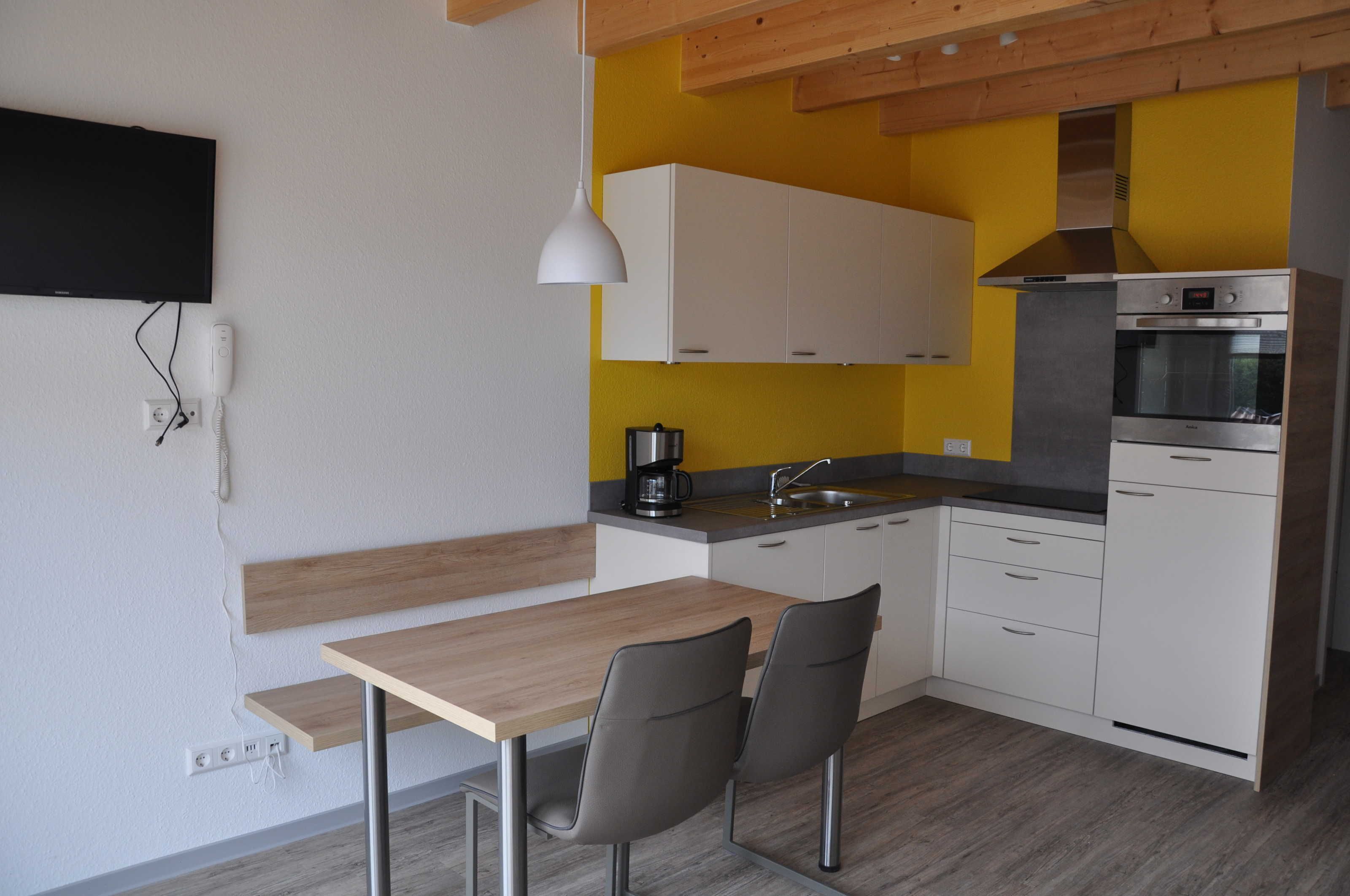 Una cucina moderna con mobili bianchi, un piano di lavoro in legno, forno integrato e macchina per il caffè.