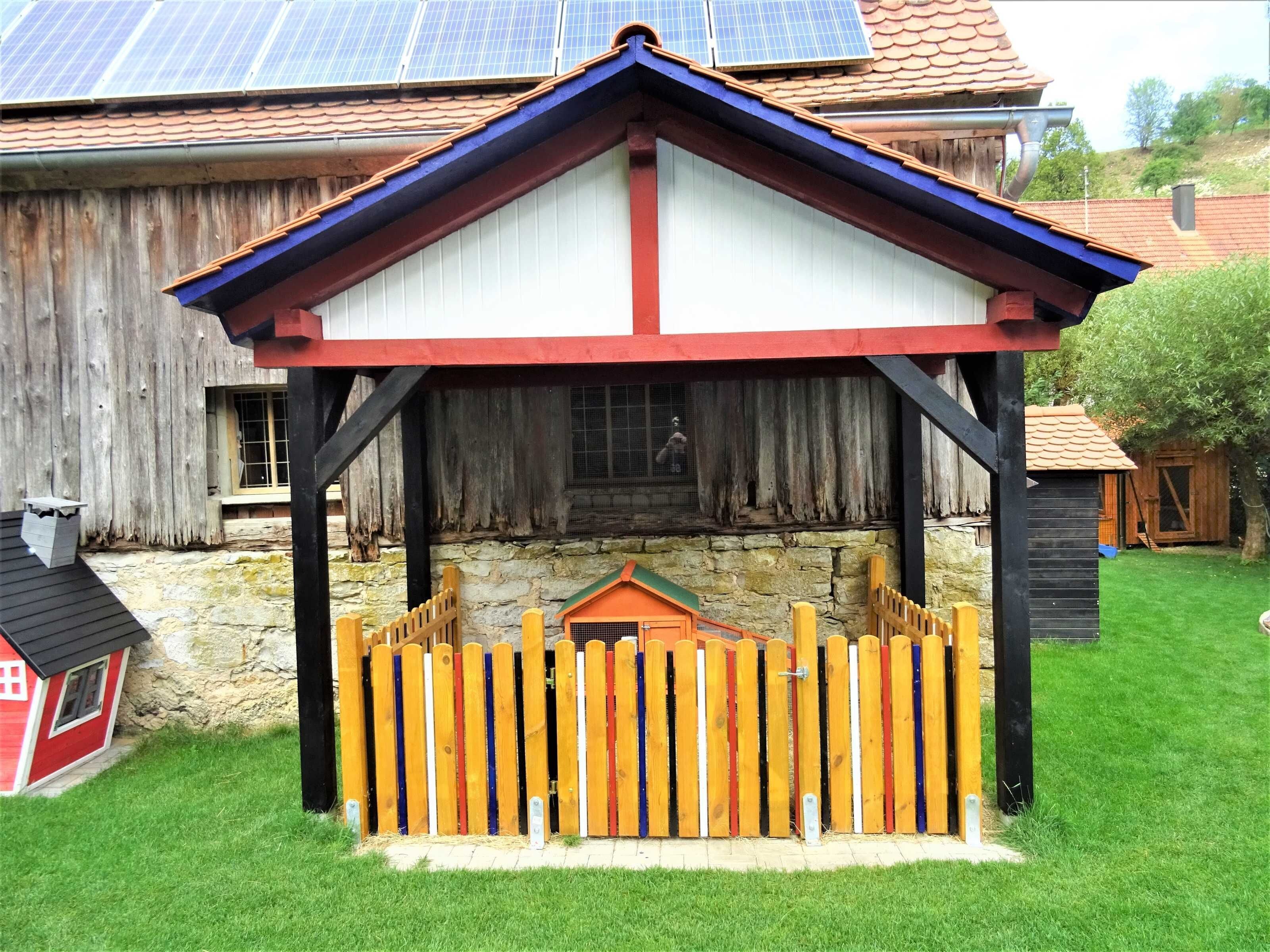 A wooden structure with a sloped roof, a stone wall, and a colorful fence.