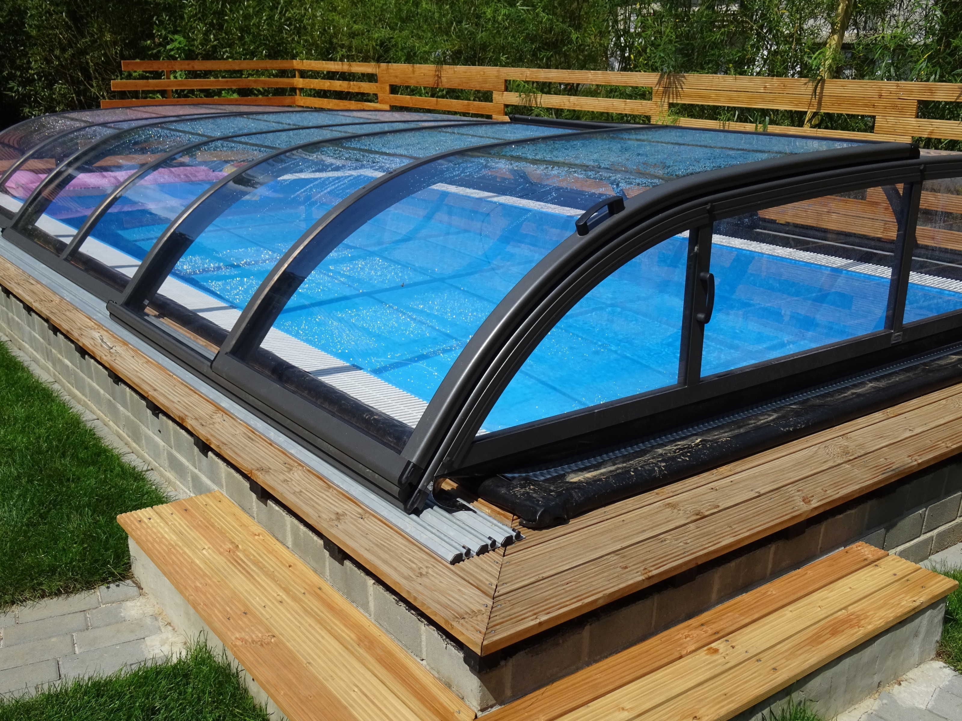 Une piscine dotée d’une enceinte en verre, d’escaliers en bois et d’une clôture en bois en arrière-plan.