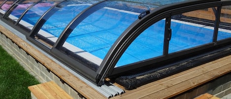 Une piscine dotée d’une enceinte en verre, d’escaliers en bois et d’une clôture en bois en arrière-plan.