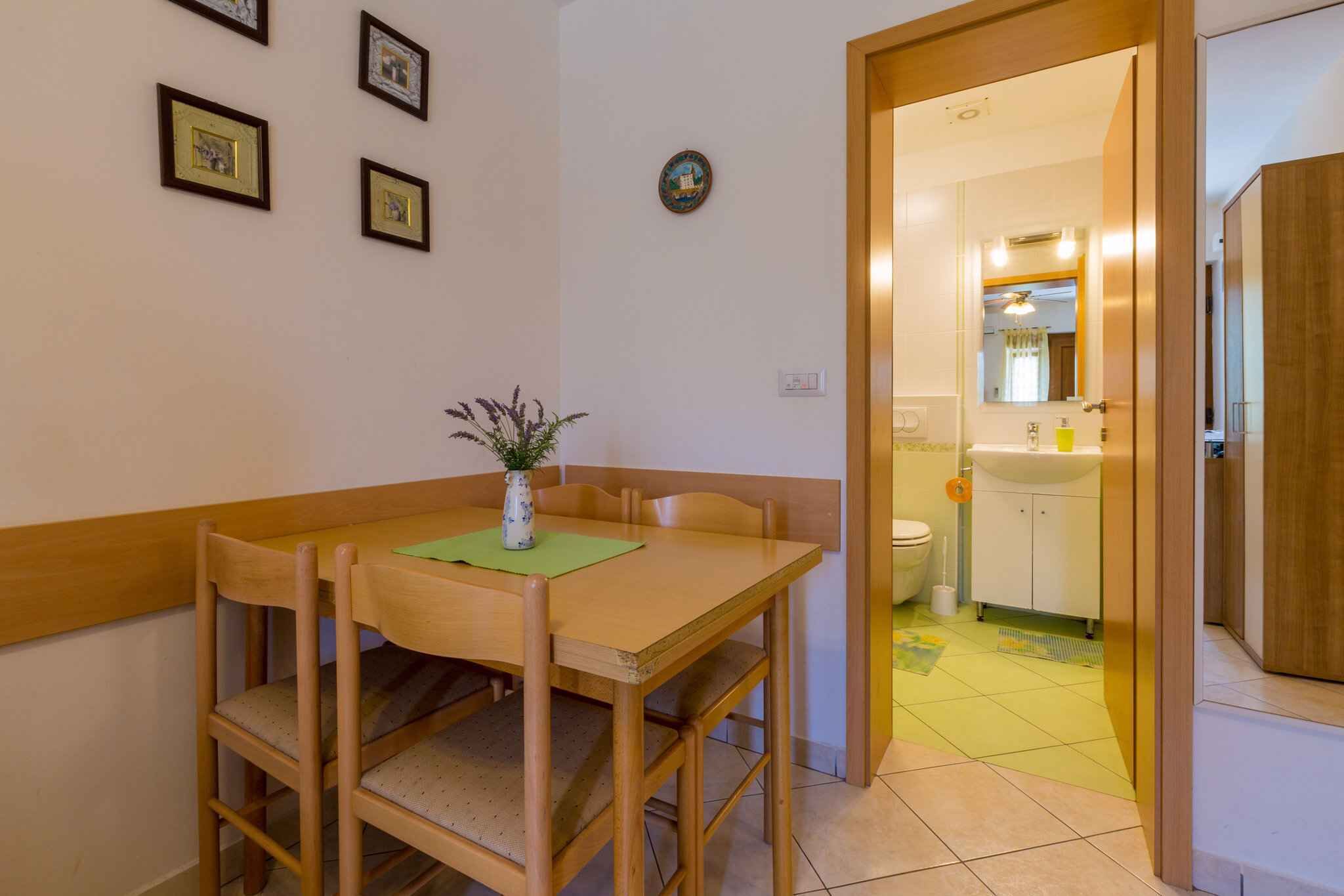 A dining area with a wooden table and chairs, a vase with a plant, and a wall with framed pictures.