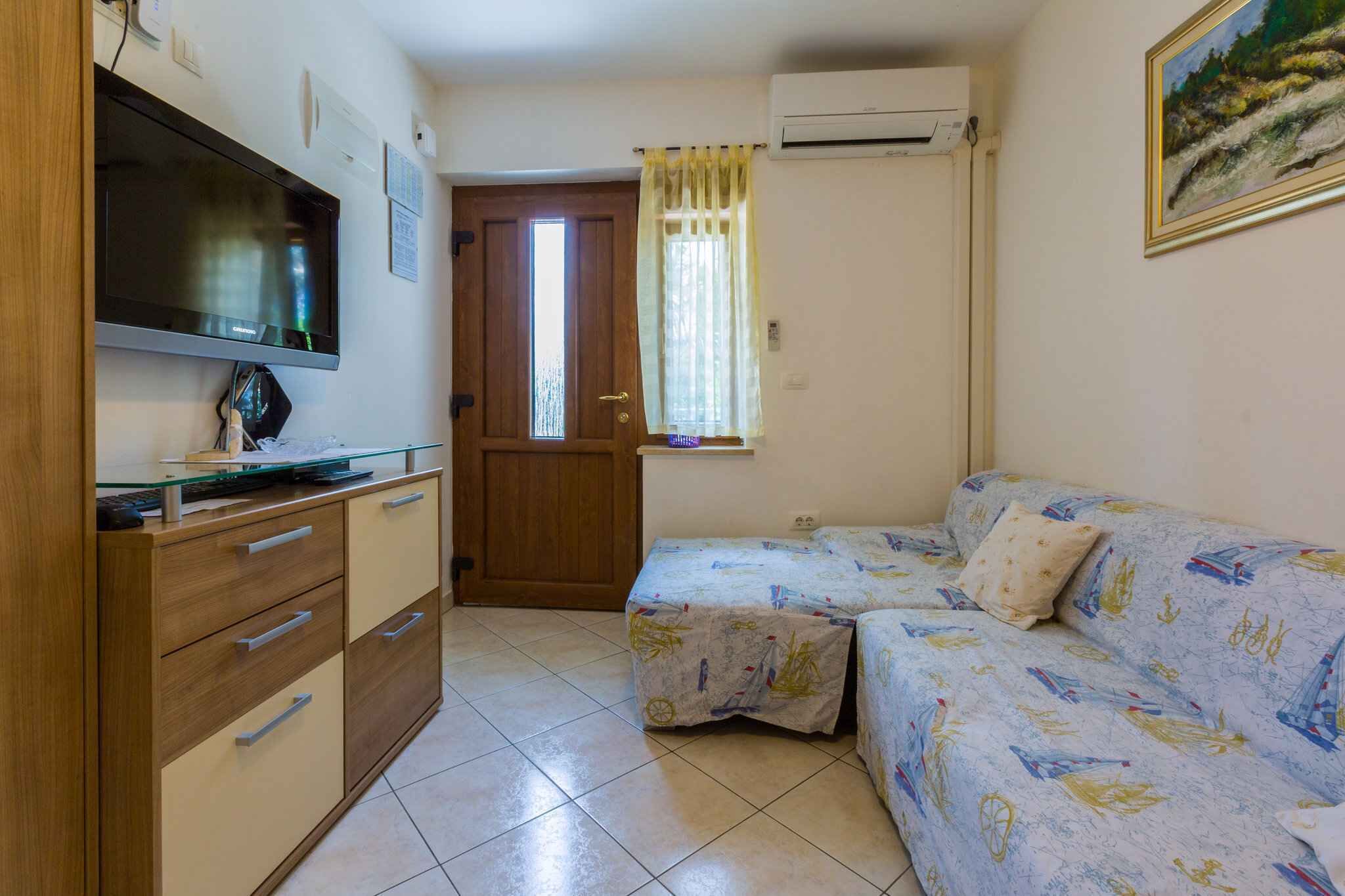 A small room with a bed, a desk with a computer, a television, and a door.